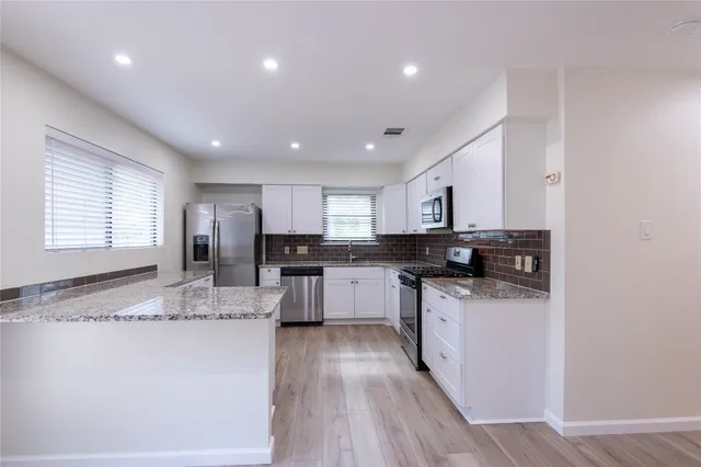 a kitchen with stainless steel appliances granite countertop a stove top oven a sink a refrigerator and white cabinets with wooden floor