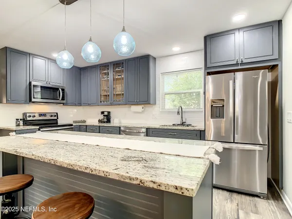 a kitchen with granite countertop a refrigerator a sink stainless steel appliances and cabinets