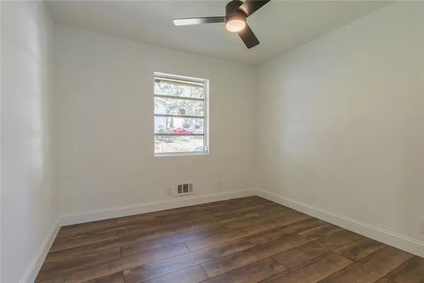 an empty room with wooden floor fan and windows