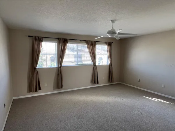 an empty room with chandelier fan and windows