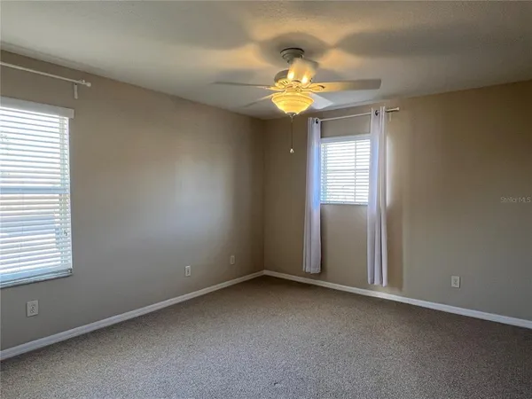 an empty room with a chandelier fan and windows