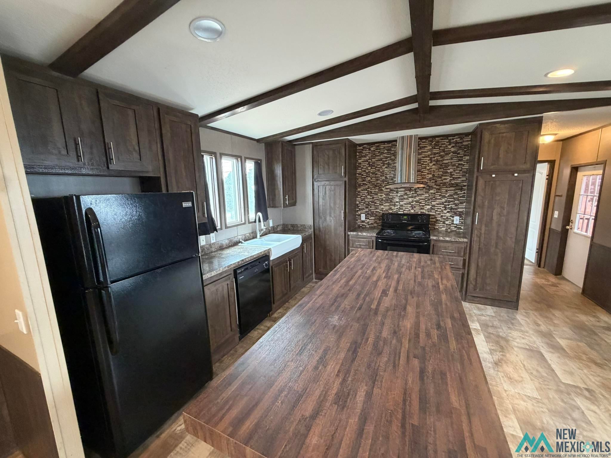 801 Riata Road Carlsbad, NM 88220 - Photo 12 of 39 Kitchen featuring a large wood-finish island, dark wood-finish cabinetry, a white farmhouse sink, and a tile backsplash
