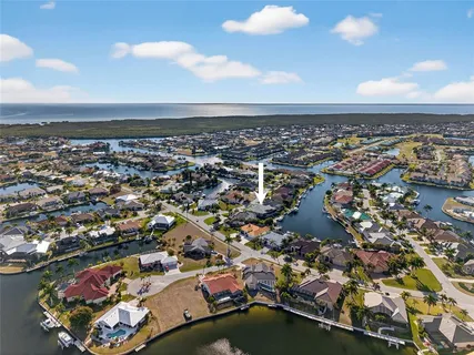 a view of a white house next to a yard with plants and large trees