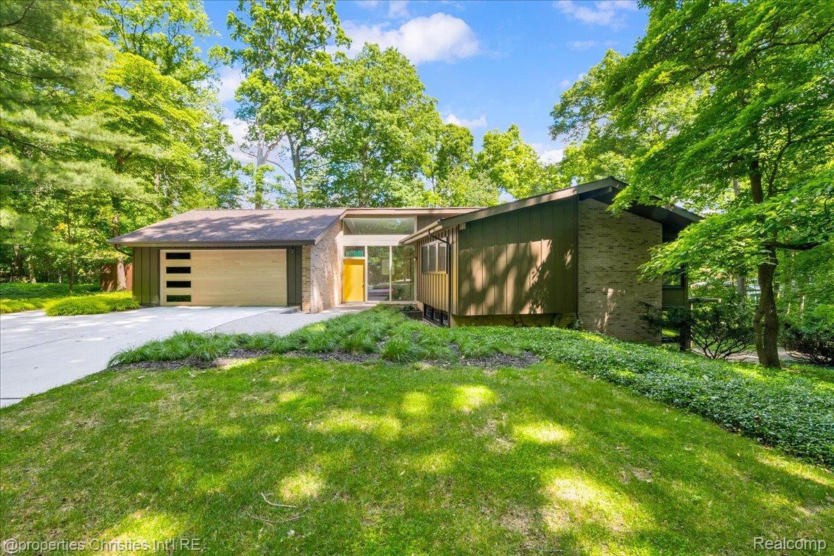 3939 Charing Cross Road Bloomfield Hills, MI 48304 - Photo 1 of 33 Contemporary residence featuring a wood-finish garage door with horizontal windows, a prominent stone facade element, and an inviting yellow entry door