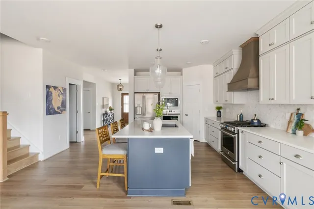 a large kitchen with stainless steel appliances kitchen island granite countertop a stove a sink a refrigerator and white cabinets with wooden floor