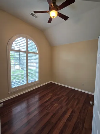 an empty room with wooden floor fan and windows