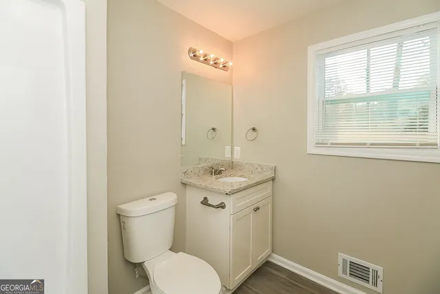 a bathroom with a granite countertop toilet a sink and a window