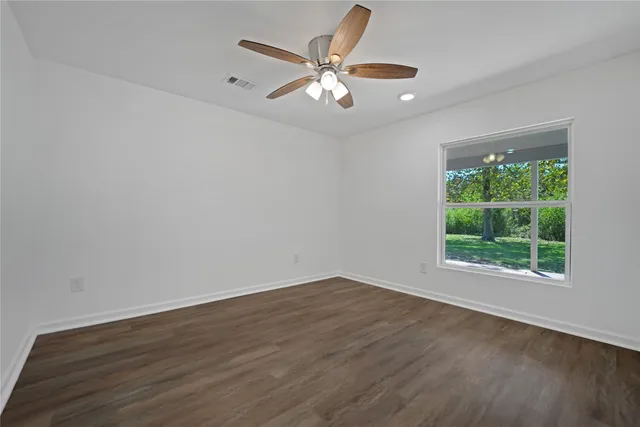 an empty room with wooden floor fan and windows