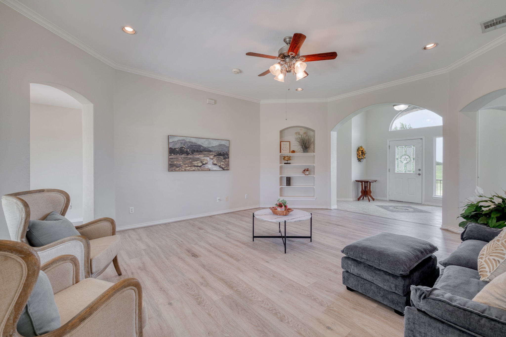 341 Brown Road McDade, TX 78650 - Photo 10 of 38 A living area with light wood flooring features built-in shelving and an arched entry, leading to the main entrance.