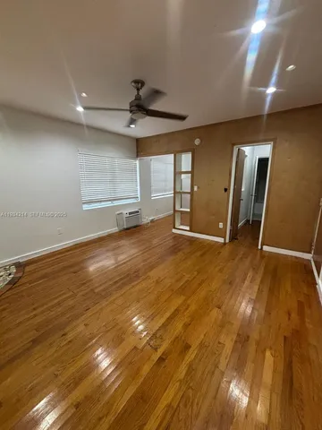 a view of an empty room with wooden floor and a ceiling fan