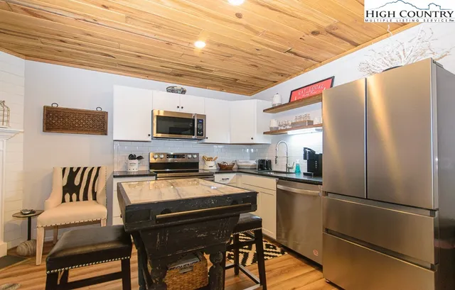 a kitchen with stainless steel appliances a refrigerator a stove a microwave oven a sink dishwasher a dining table and chairs with wooden floor