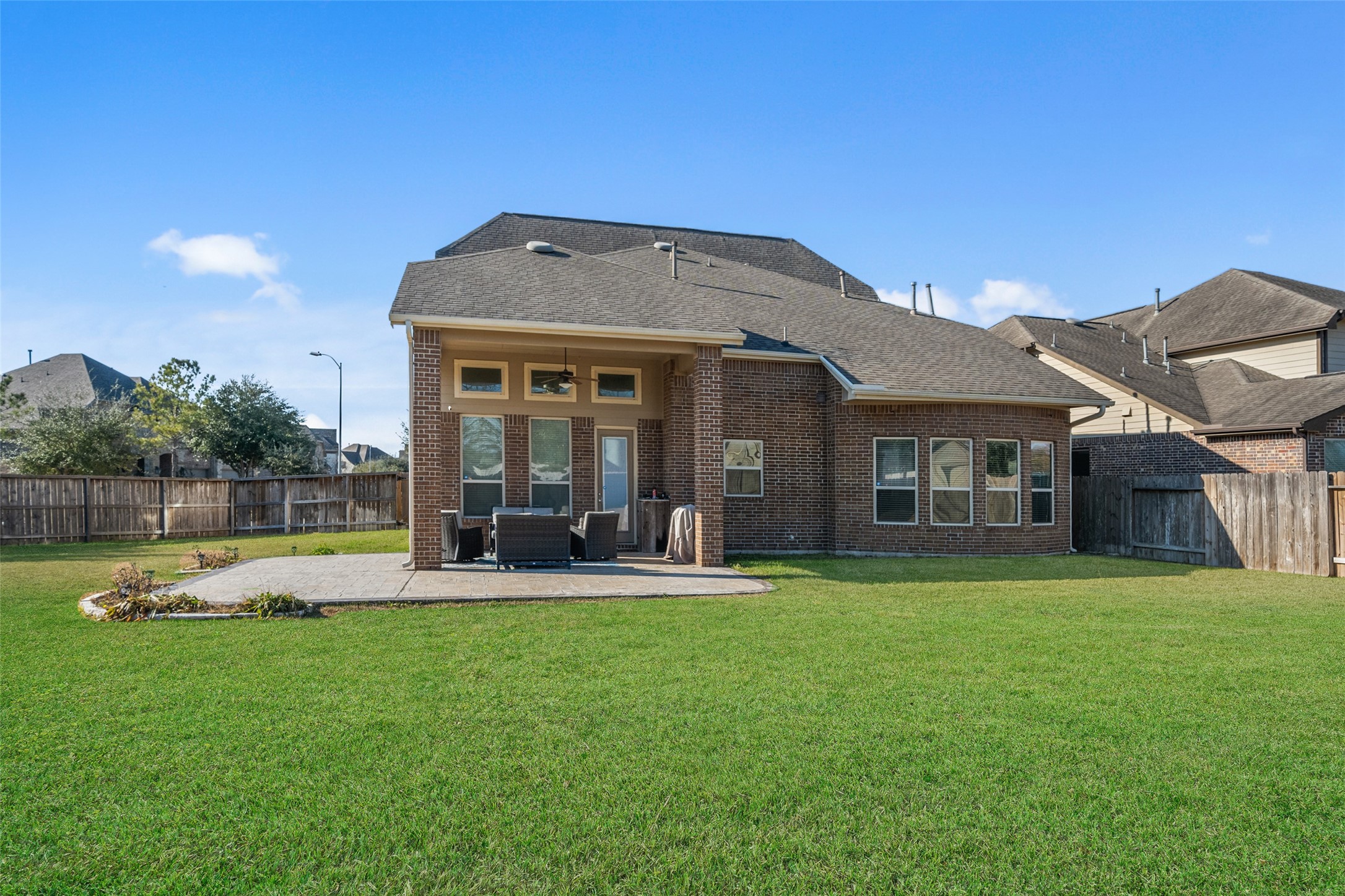 4747 Abercorn Street Rosharon, TX 77583 - Photo 32 of 46 This photo showcases a spacious backyard with a well-maintained lawn and a cozy patio area. The brick exterior of the house features large windows and a covered patio, offering a great space for outdoor entertaining. The fenced yard provides privacy, ideal for families or pets.