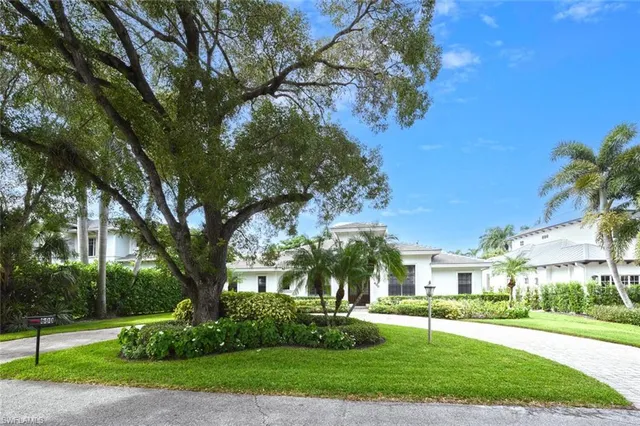 a view of a white house next to a yard with big trees