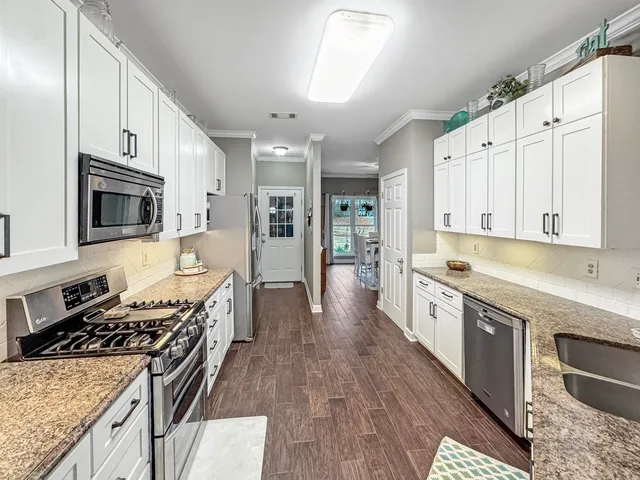 a large kitchen with stainless steel appliances granite countertop a stove top oven a sink dishwasher and white cabinets with wooden floor