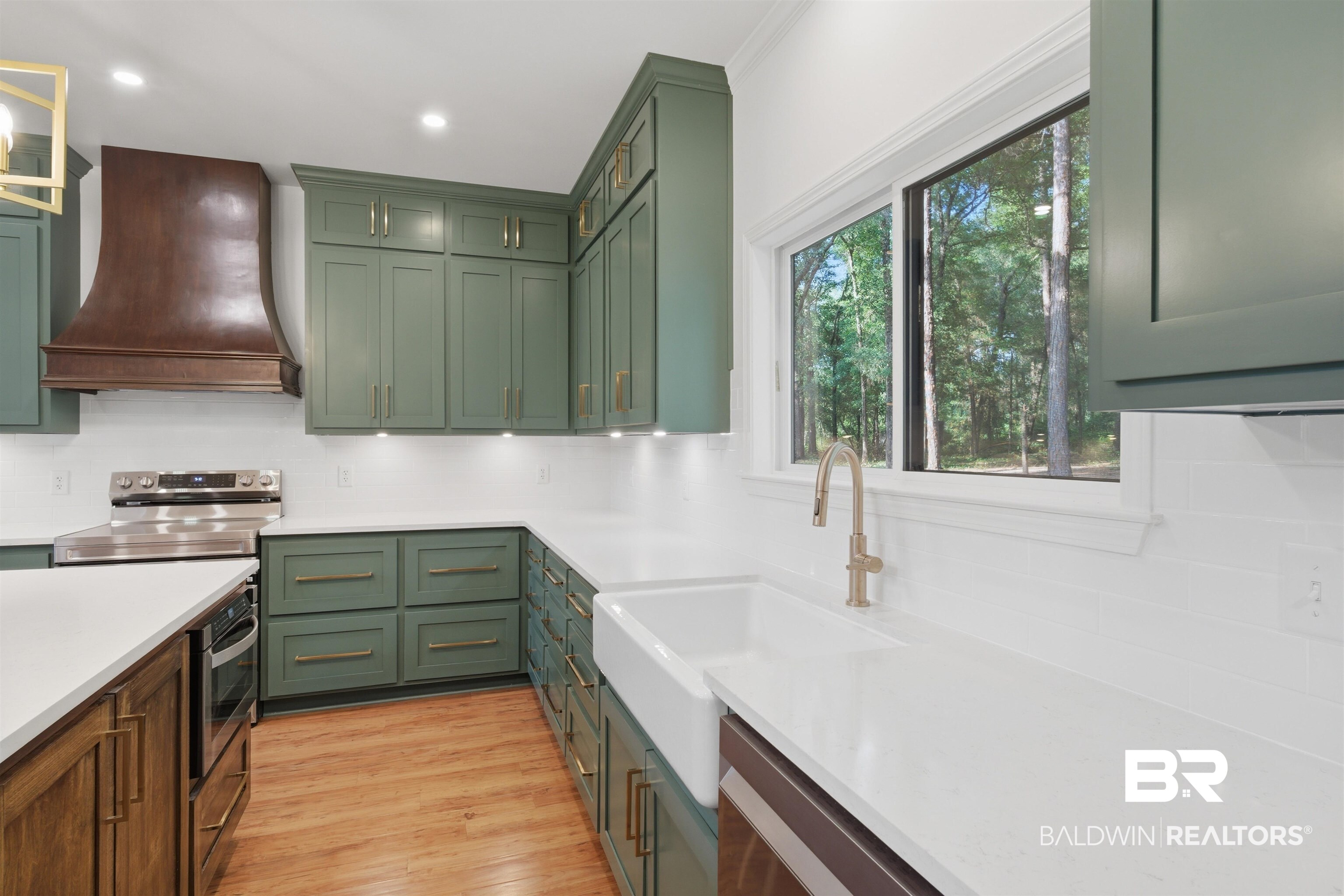 14128 Jackson Lane Foley, AL 36535 - Photo 10 of 36 Kitchen featuring sage green cabinetry, white countertops, a farmhouse sink with a gold-tone faucet, wood-finish flooring, and a window overlooking mature trees
