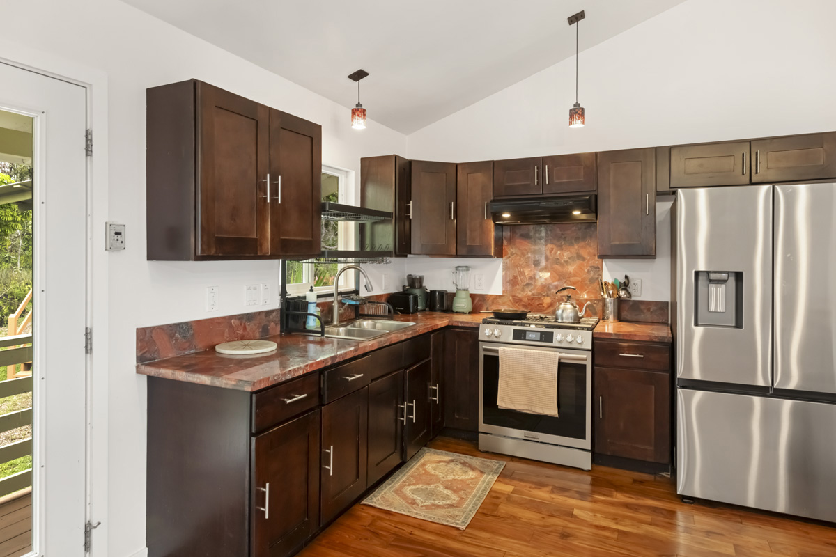 12-1098 Kaimu-Makena Homestead Road Pahoa, HI 96778 - Photo 17 of 29 a kitchen with stainless steel appliances granite countertop a refrigerator a sink dishwasher a stove and white cabinets with wooden floor