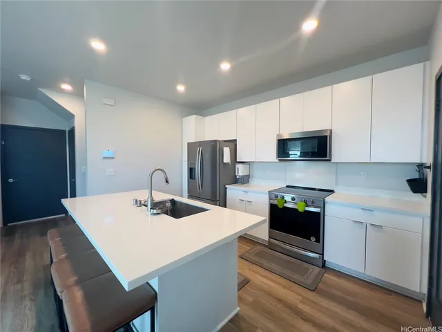 a kitchen with stainless steel appliances kitchen island granite countertop a sink dishwasher a stove a refrigerator with white cabinets and wooden floor