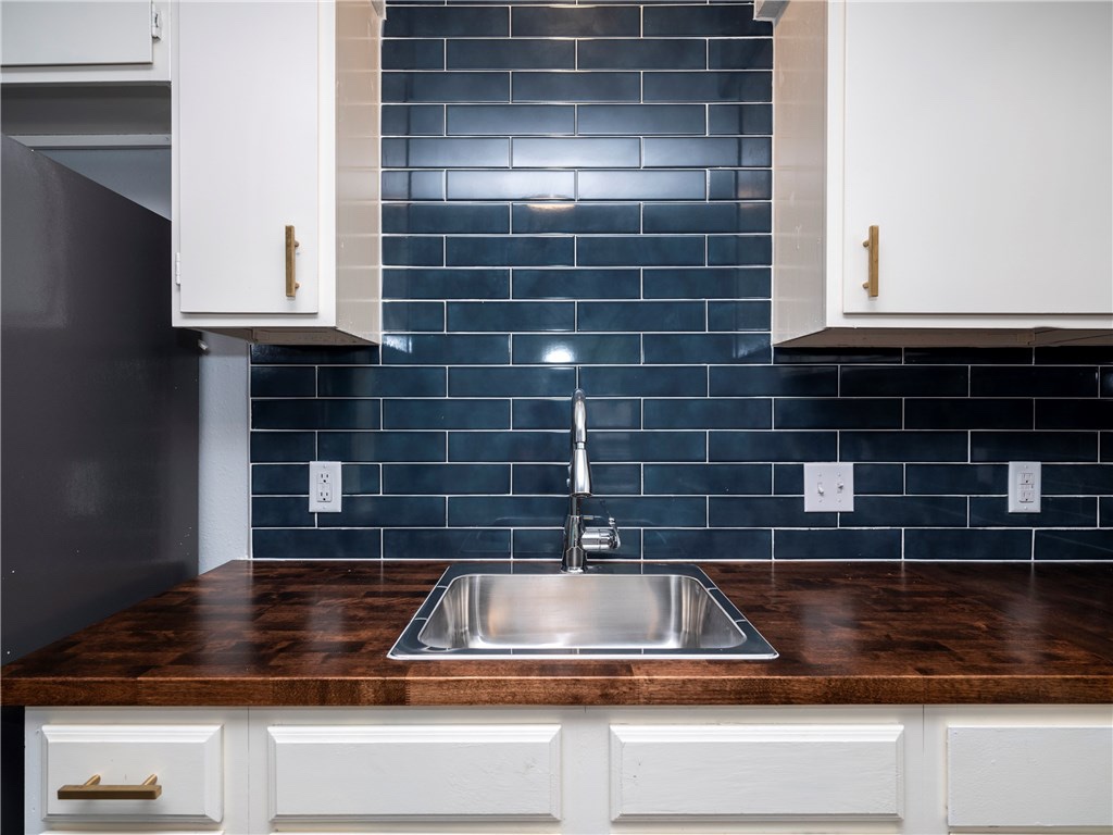 7004 Circle S Road, Unit B Austin, TX 78745 - Photo 4 of 12 A deep blue subway tile backsplash highlights a sleek stainless steel sink and warm wood countertops.