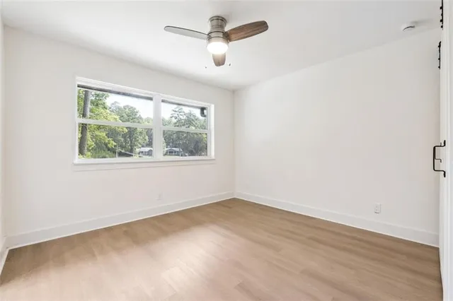 an empty room with wooden floor ceiling fan and windows