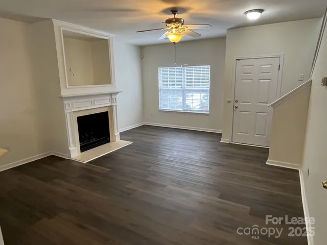 an empty room with wooden floor a ceiling fan a fireplace and windows
