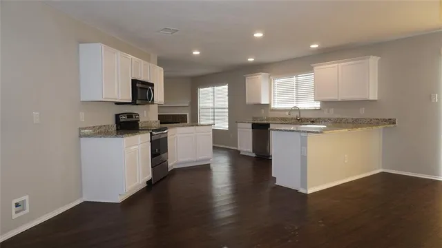 a kitchen with stainless steel appliances granite countertop a stove top oven a sink a window and white cabinets