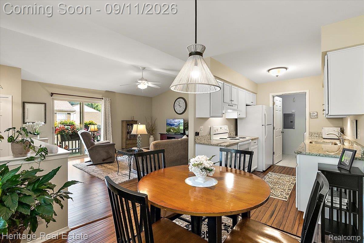 Open-concept living space featuring wood-finish flooring, a kitchen with granite countertops, white cabinetry, and a ceiling fan in the living area