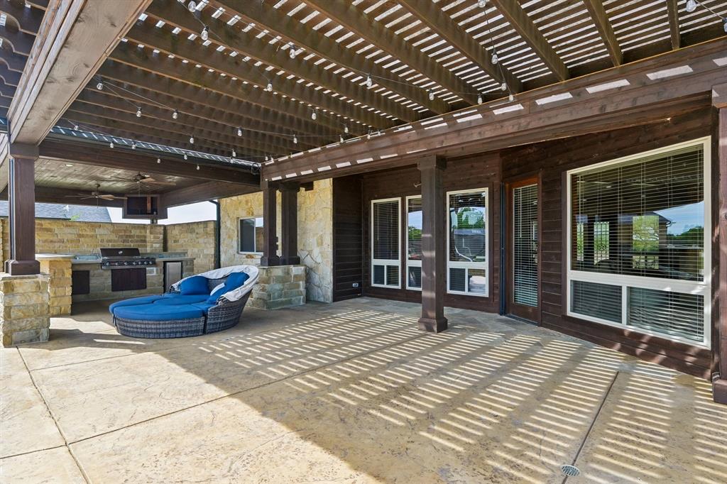 2085 Switzer Road Sanger, TX 76266 - Photo 31 of 39 Expansive covered patio featuring a full outdoor kitchen, stamped concrete flooring, a pergola with string lighting, stone accent pillars, and multiple large windows