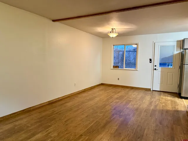 a view of an empty room with wooden floor and a window