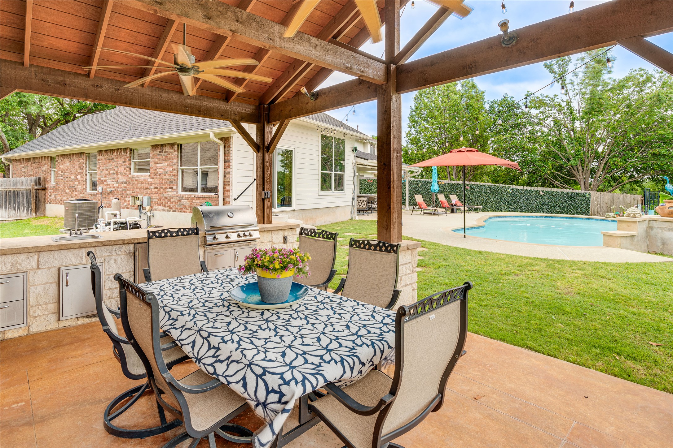 1209 Lacey Oak Loop Round Rock, TX 78681 - Photo 7 of 22 Expansive covered patio featuring an outdoor kitchen with built-in grill and sink, wood-beamed ceiling with ceiling fans, and concrete patio flooring