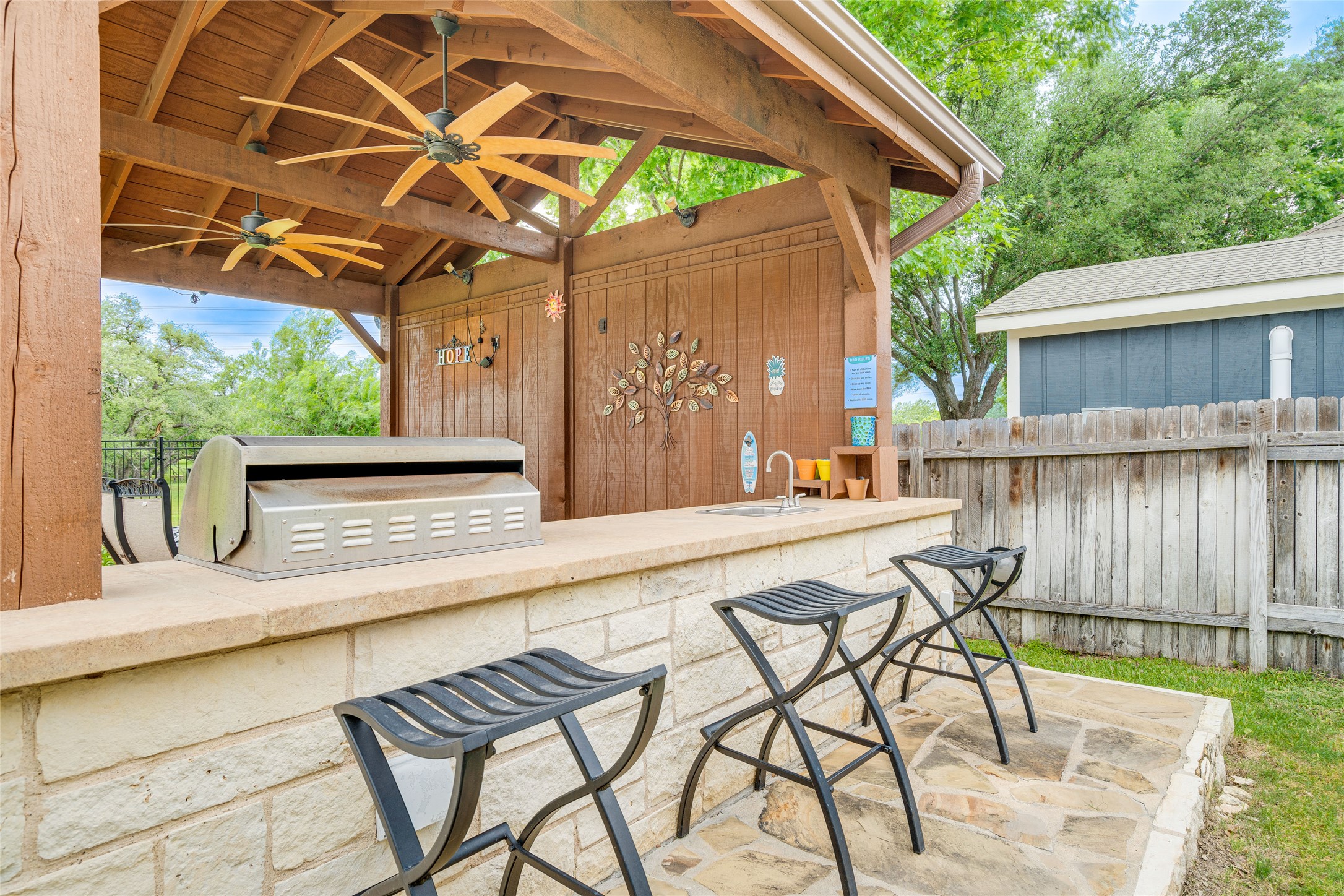 1209 Lacey Oak Loop Round Rock, TX 78681 - Photo 9 of 22 Covered outdoor kitchen featuring a built-in grill, integrated sink, stone veneer bar, and wood-finish ceiling with dual ceiling fans