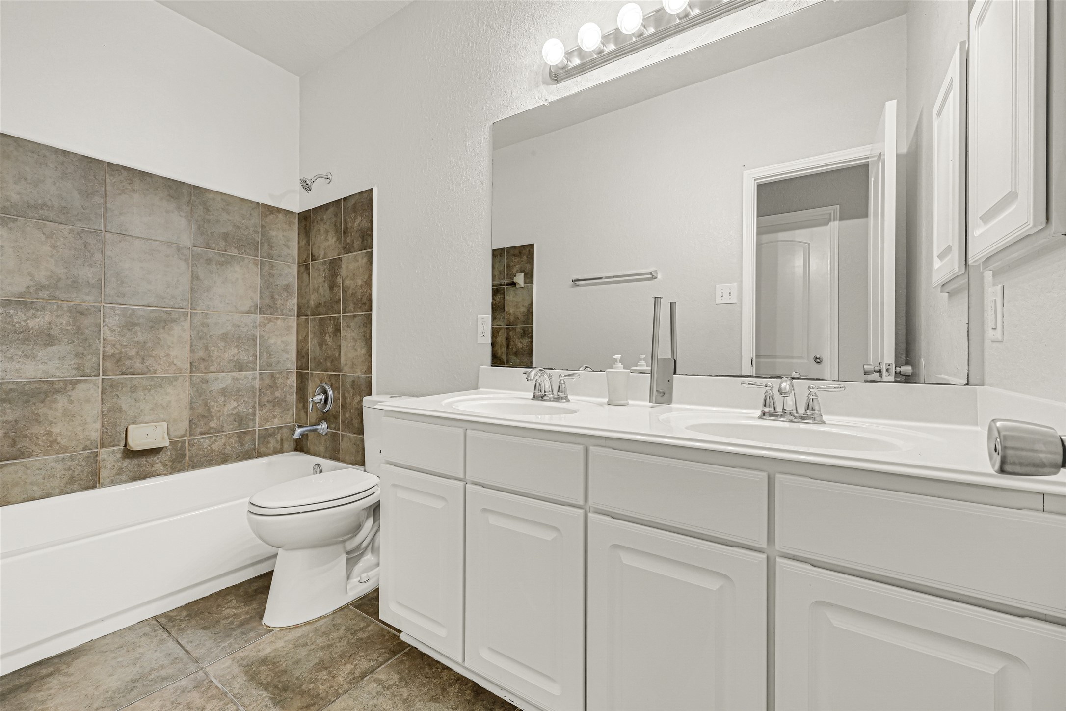 4702 Sedgewood Drive Rosenberg, TX 77471 - Photo 7 of 24 This is a spacious bathroom featuring a large double vanity with white cabinetry, ample counter space, and a wide mirror. The room is well-lit with modern fixtures and has a neutral color palette. The floor is tiled, and there's a glimpse of a tiled shower area.
