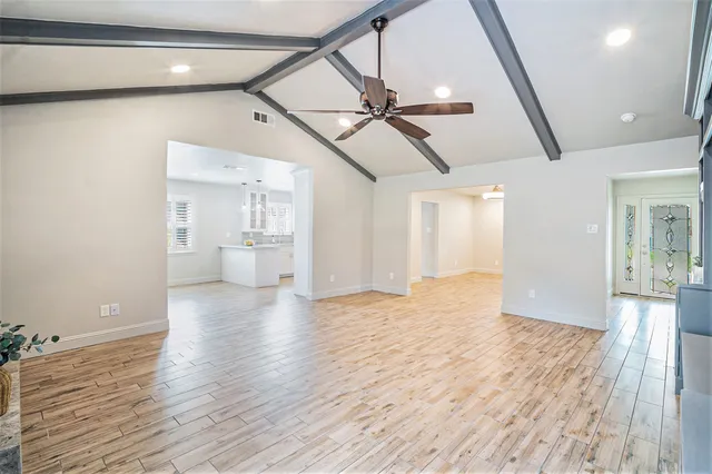 a view of an empty room with wooden floor and a kitchen