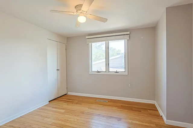 an empty room with wooden floor fan and windows