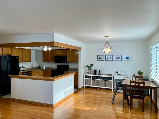 a kitchen with stainless steel appliances a microwave a stove a refrigerator a dining table and chairs with wooden floor