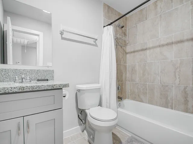 a bathroom with a granite countertop bathtub shower sink vanity and toilet