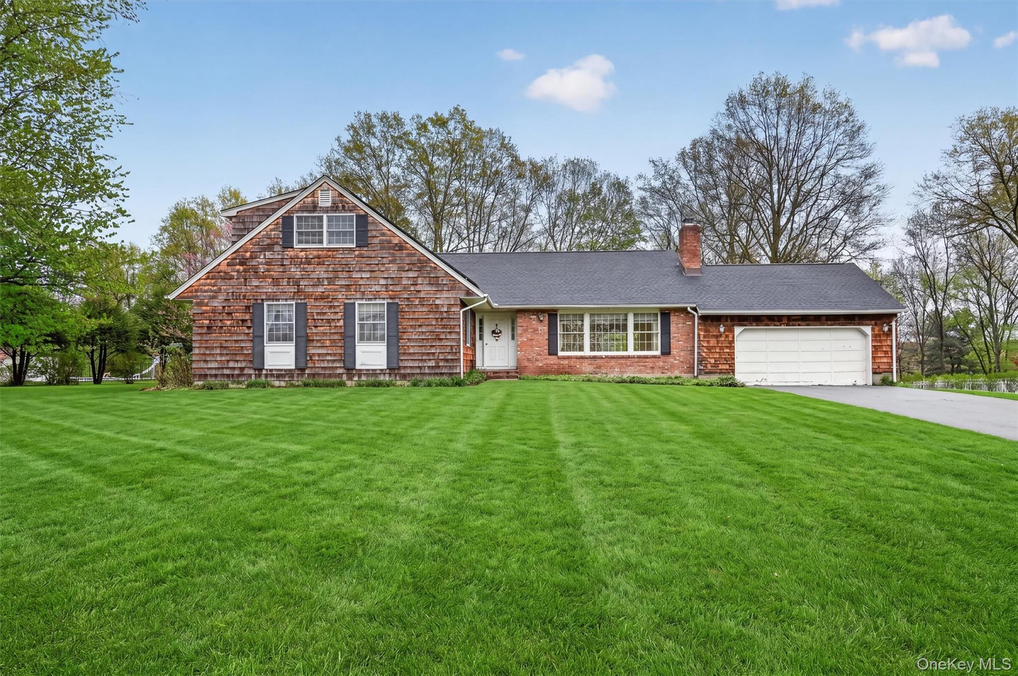 Expansive green lawn with a traditional-style residence featuring cedar shake siding and brick accents