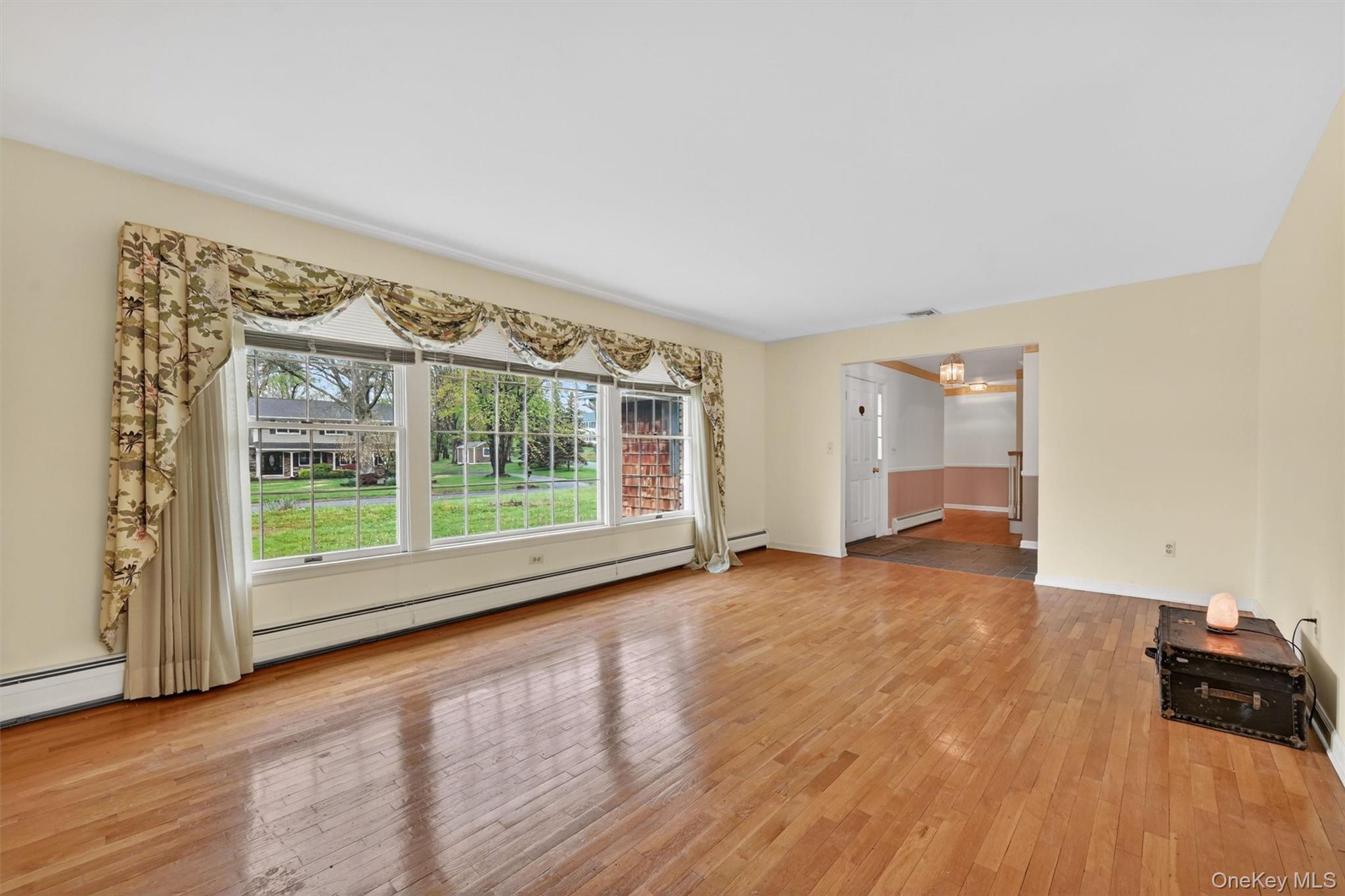 16 Ridgeview Terrace Goshen, NY 10924 - Photo 6 of 35 Spacious room featuring wood-finish flooring, a large multi-pane window overlooking a green exterior, and a wide doorway opening to an additional room