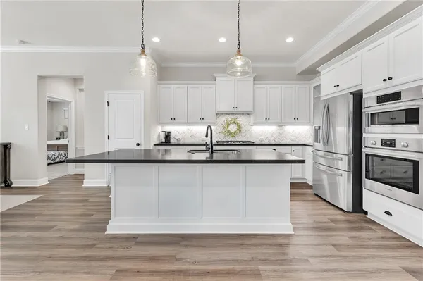 a kitchen with stainless steel appliances granite countertop a stove a refrigerator a sink and white cabinets with wooden floor