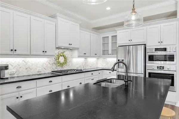 a kitchen with granite countertop a refrigerator a stove a sink and white cabinets with wooden floor