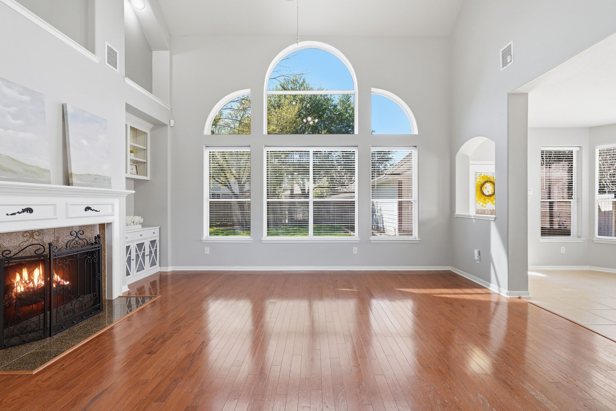 24931 Corbin Gate Drive Spring, TX 77389 - Photo 12 of 50 This spacious living room features high ceilings, large arched windows for ample natural light, a cozy fireplace, and beautiful hardwood floors, creating a warm and inviting atmosphere.