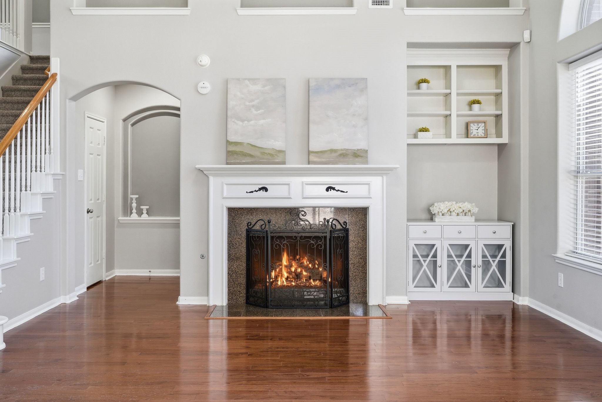 24931 Corbin Gate Drive Spring, TX 77389 - Photo 13 of 50 This elegant living room features a cozy fireplace with built-in shelving and cabinetry. The open layout includes hardwood floors, large windows for natural light, and a staircase leading to the upper level. Neutral tones create a bright, inviting atmosphere.