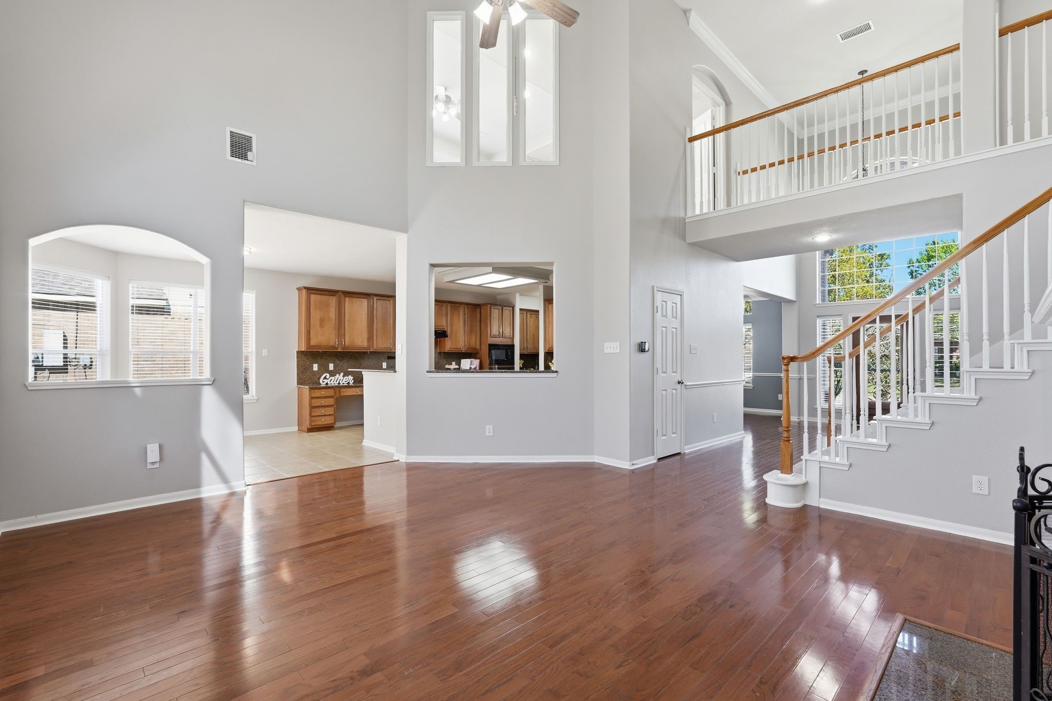 24931 Corbin Gate Drive Spring, TX 77389 - Photo 16 of 50 This spacious, open-concept home features high ceilings and abundant natural light. The living area seamlessly connects to a modern kitchen with wooden cabinetry. A grand staircase leads to an upper level, accented by elegant railings.