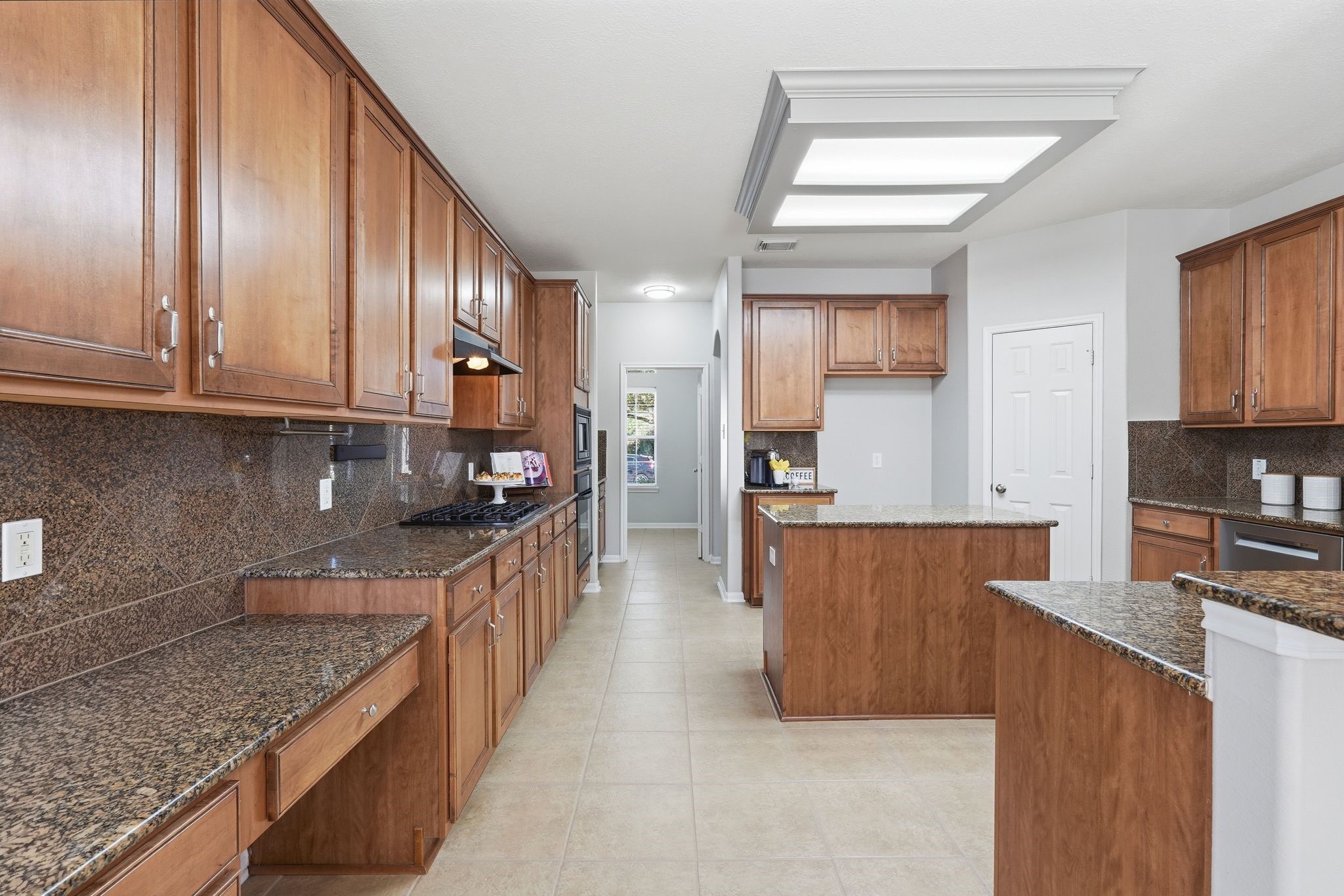 24931 Corbin Gate Drive Spring, TX 77389 - Photo 19 of 50 This spacious kitchen features elegant wood cabinetry, granite countertops, and a central island. The room offers ample storage and workspace, with modern appliances and a sleek tile floor, providing a warm and functional cooking environment.