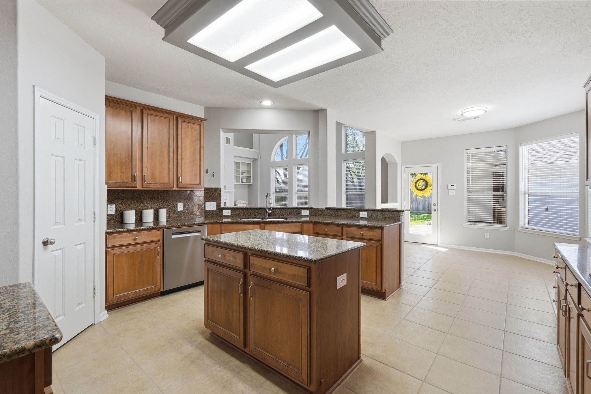 24931 Corbin Gate Drive Spring, TX 77389 - Photo 21 of 50 This spacious kitchen features warm wood cabinetry, granite countertops, and modern stainless steel appliances. It opens into a bright dining area with large windows and a door leading to the backyard, providing ample natural light.