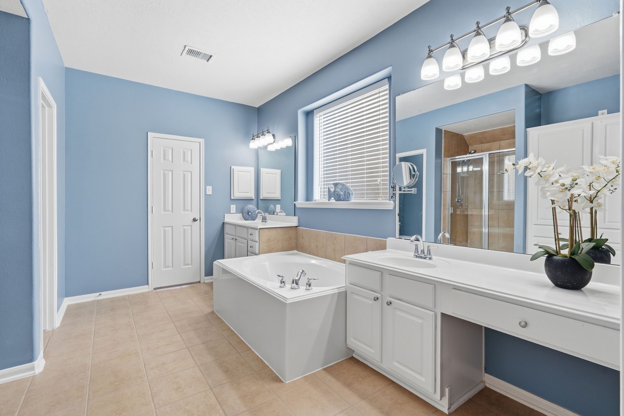 24931 Corbin Gate Drive Spring, TX 77389 - Photo 35 of 50 This primary bathroom features a relaxing soaking tub, dual sinks, and a separate walk in shower. The soft blue walls and ample lighting create a serene atmosphere, complemented by elegant fixtures and a large window for natural light.
