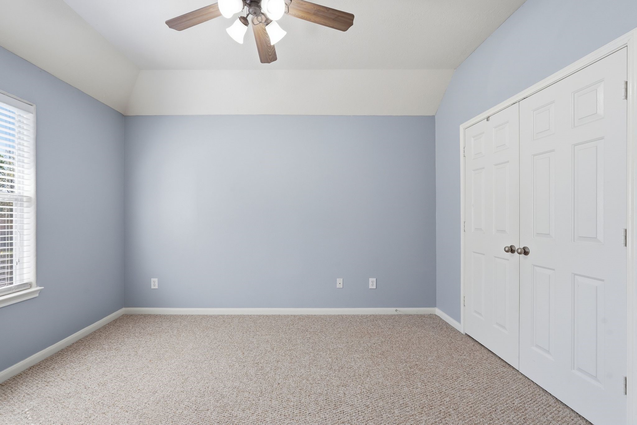 24931 Corbin Gate Drive Spring, TX 77389 - Photo 39 of 50 This upstairs secondary bedroom features soft blue walls, a beige carpet, and a ceiling fan. It includes a window with blinds, allowing natural light, and a double-door closet for storage.