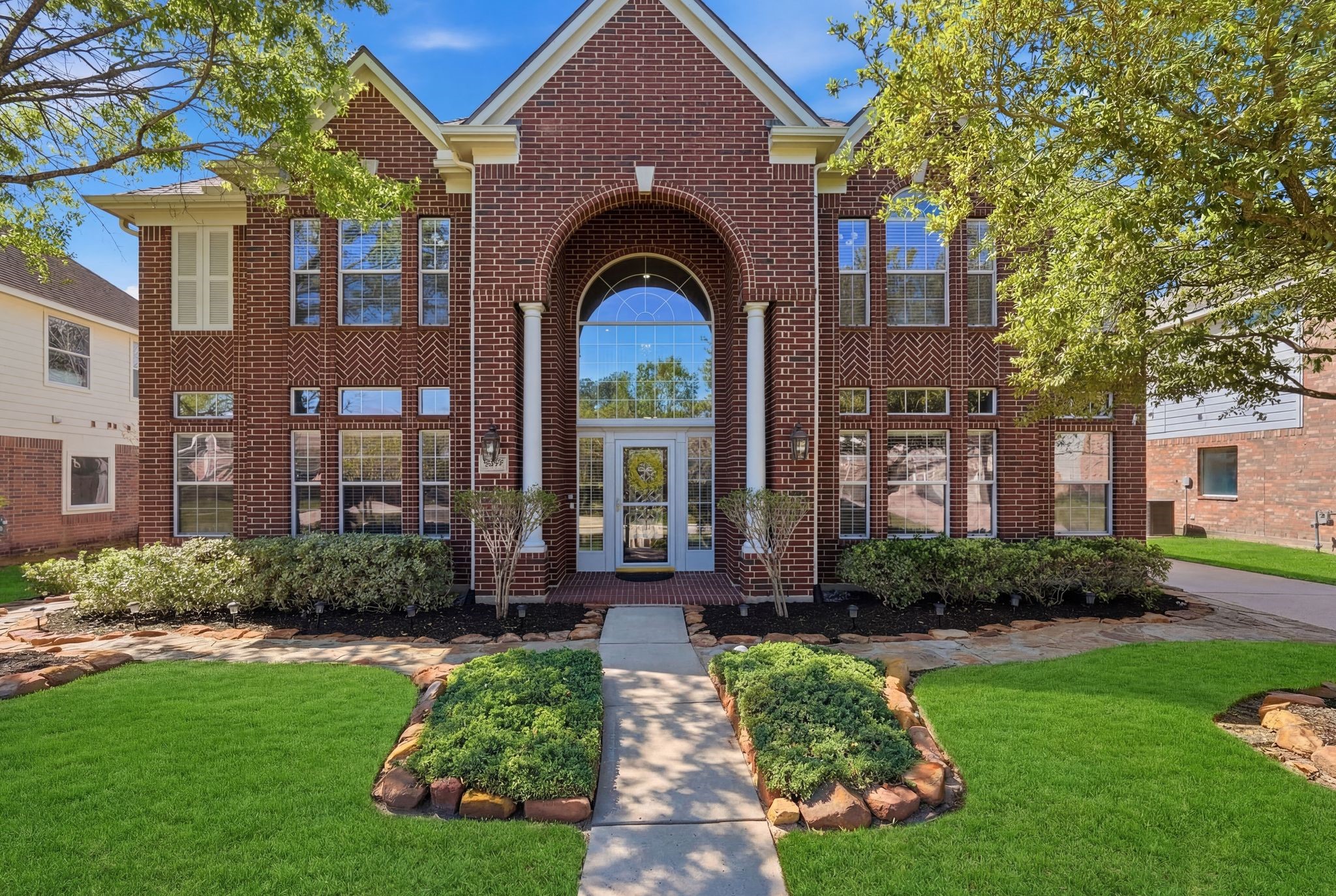 24931 Corbin Gate Drive Spring, TX 77389 - Photo 4 of 50 This beautiful home features a grand entrance with large arched windows and a well-maintained front yard. The path leads through lush greenery, offering excellent curb appeal in Auburn Lakes.