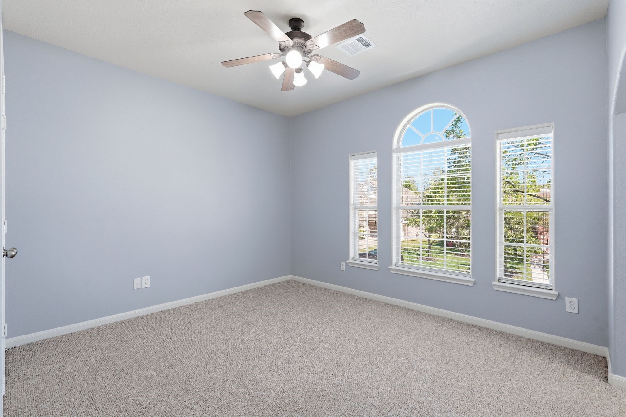 24931 Corbin Gate Drive Spring, TX 77389 - Photo 41 of 50 This secondary bedroom features neutral walls and a carpeted floor, with ample natural light streaming through three large windows, including a stylish arched design. A ceiling fan adds comfort and functionality.