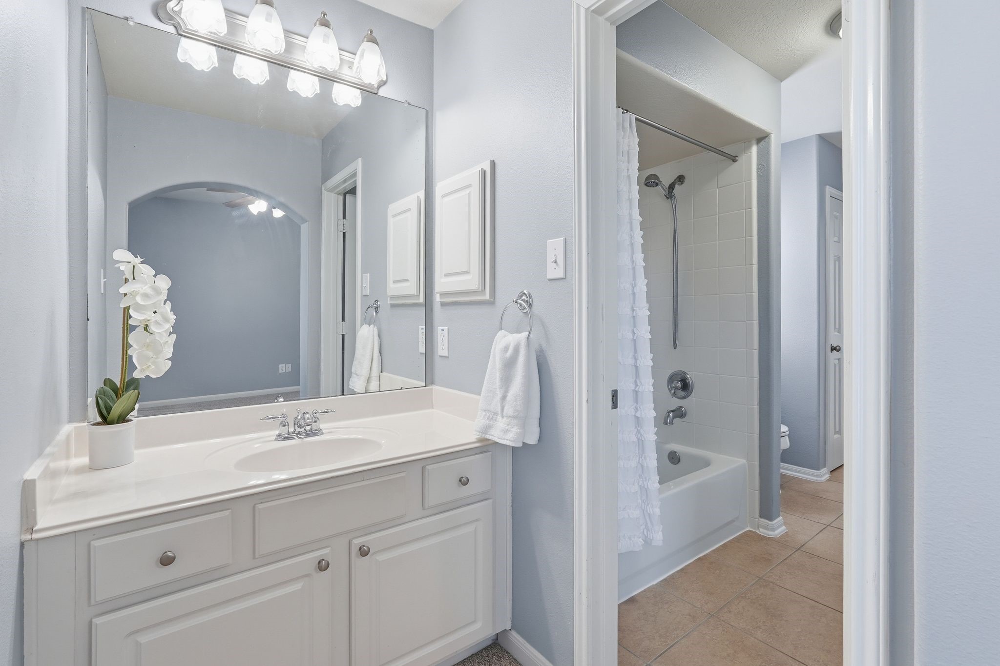 24931 Corbin Gate Drive Spring, TX 77389 - Photo 42 of 50 The jack and jill bathroom features a clean, bright design with a large mirror, stylish vanity with storage, and a combined shower-tub with a white tile surround. The neutral colors and modern lighting create a fresh and inviting atmosphere.