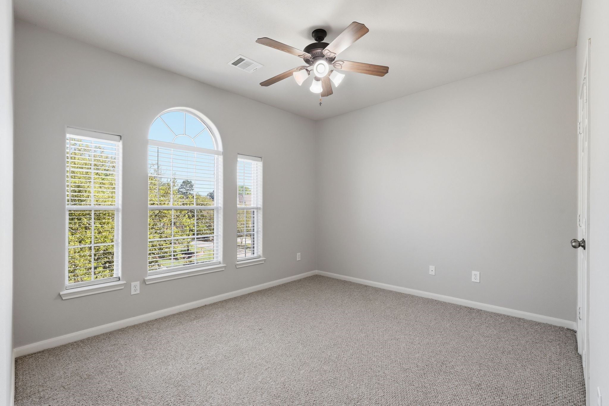 24931 Corbin Gate Drive Spring, TX 77389 - Photo 43 of 50 Bright secondary bedroom with neutral carpeting, soft gray walls, and a ceiling fan. Features three large windows with an arched top, offering plenty of natural light and a pleasant view of the front of the house.